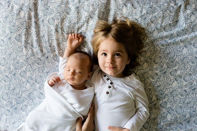 zwei Kinder liegen Arm in Arm, Baby und 4 Jahre