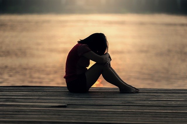 Wie du dir selbst Empathie geben kannst, wenn du verletzt wurdest - junge Frau sitzt in der Dämmerung auf einem Steg und legt den Kopf auf die Knie