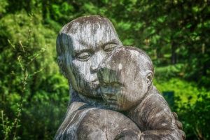 Holzskulptur: Mutter hat Kind über die Schulter, strahlt Geborgenheit, Trösten und Nähe aus