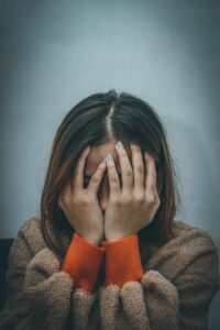 junge frau hält sich die hände vor das gesicht, im hintergrund nebel, sie hat bunte Ärmel und trägt pelzjacke