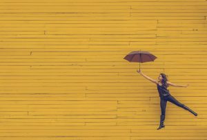 Frau schwebt mit Regenschirm vor Mauer