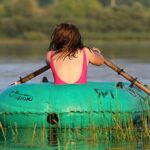 Welche Folgen haben Kindheitstraumata im Erwachsenenalter? Junge Frau im Badeanzug von hinten rudert allein in einem Gummiboot über den See