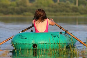 Junge Frau im Badeanzug von hinten rudert allein in einem Gummiboot über den See