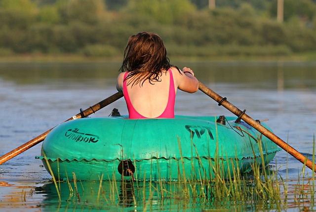 Junge Frau im Badeanzug von hinten rudert allein in einem Gummiboot über den See