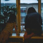 ein kind von hinten, es sitzt am fenster und schaut in die dämmerung einer stadt