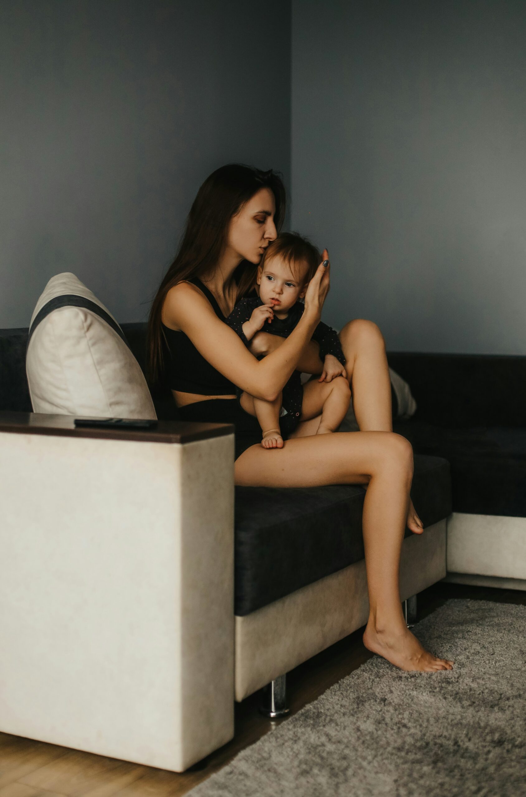 eine Frau mit nackten schlanken beinen sitzt auf dem sofa und hält ein baby im arm
