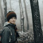 ein junge mit roter mütze im verschneiten wald, er schaut traurig und hilflos aus