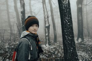 ein junge mit roter mütze im verschneiten wald, er schaut traurig und hilflos aus