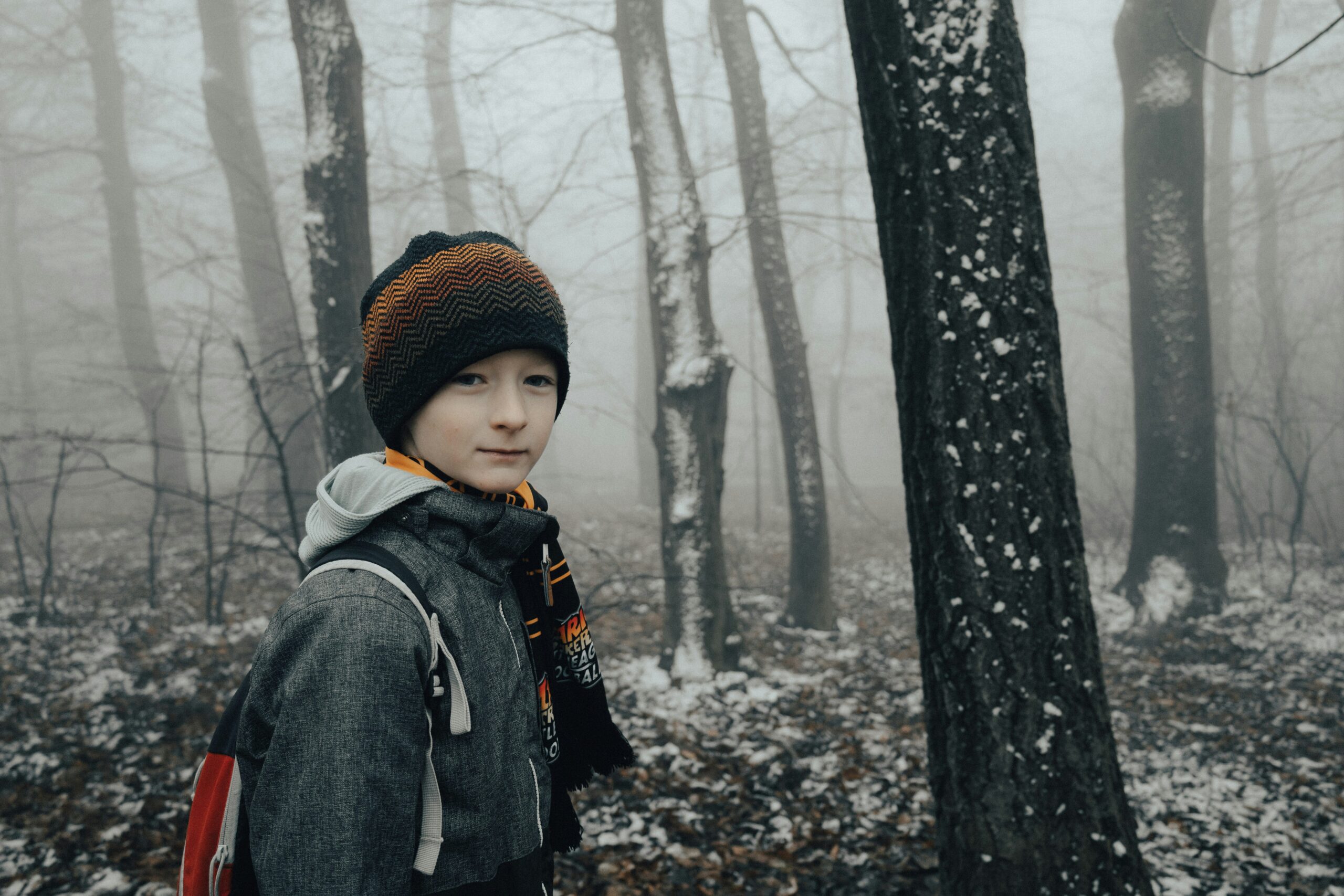 ein junge mit roter mütze im verschneiten wald, er schaut traurig und hilflos aus