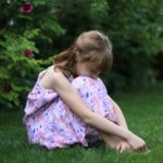 ein mädchen sitzt im garten und verbirgt das gesicht in ihren beinen, sie sieht traurig aus