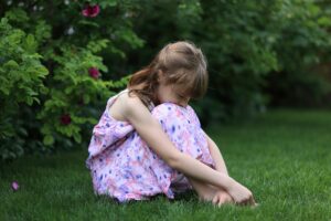 ein mädchen sitzt im garten und verbirgt das gesicht in ihren beinen, sie sieht traurig aus